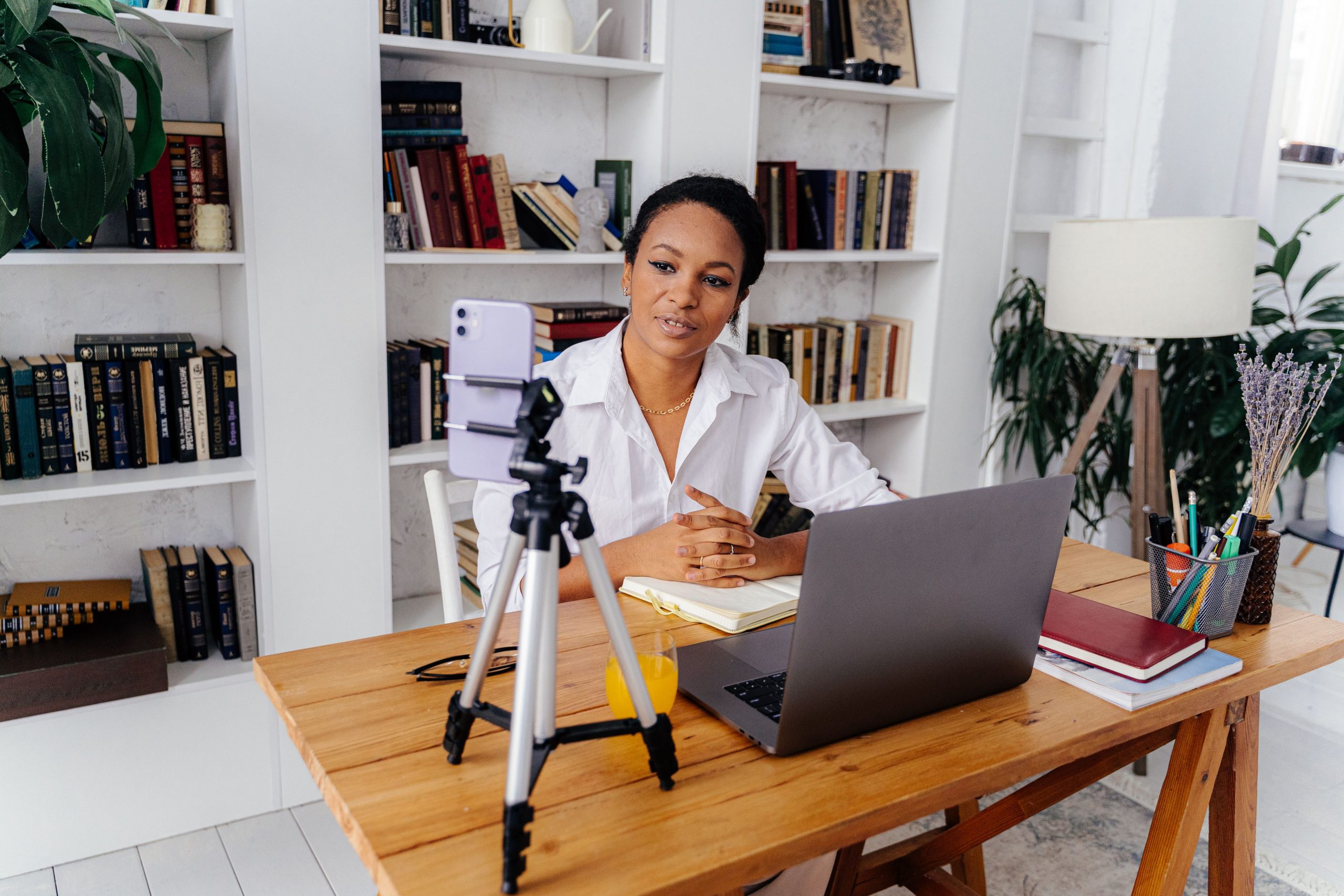 Home A woman working remotely using a laptop and smartphone in a home office setup with bookshelves.